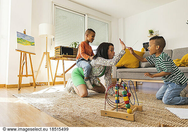 Young woman playing with twin sons in living room at home