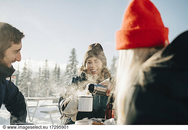 Young woman pouring coffee for female friend during winter