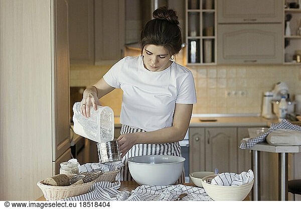 Young woman pouring flour in measuring cup
