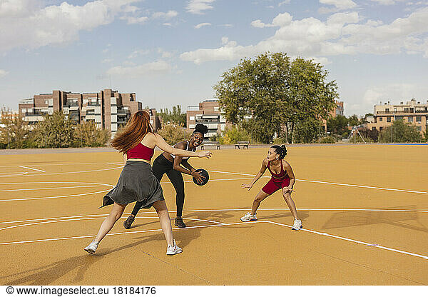 Young woman practicing basketball with friends in sports court