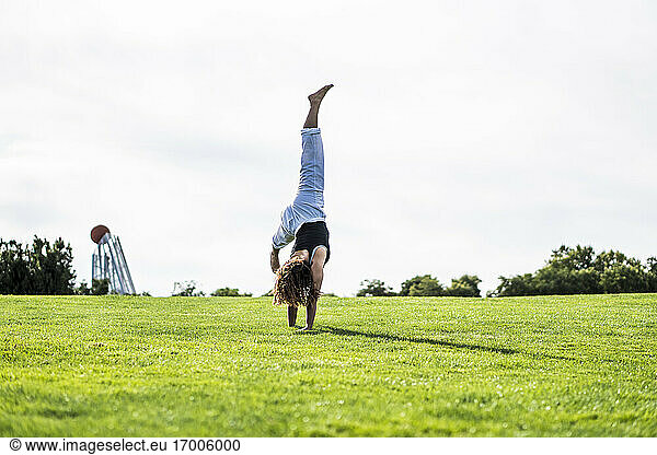 Young woman practicing cartwheel on grass against clear sky