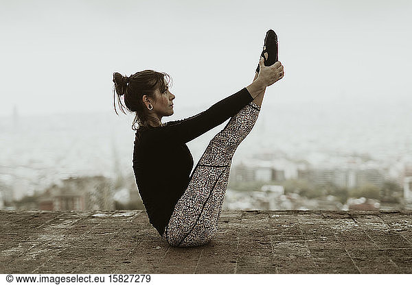 Young woman practicing yoga  asana holding her feet with her hands