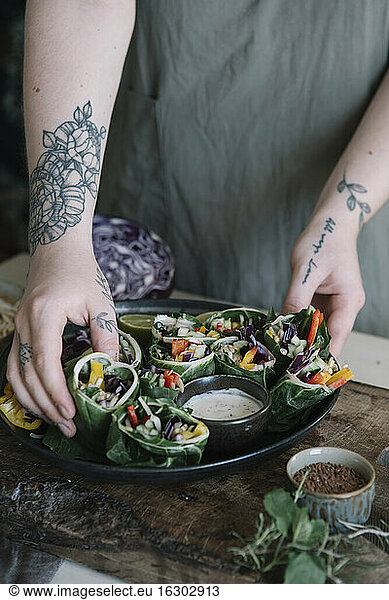 Young woman preparing vegan roll with vegetables and yoghurt sauce