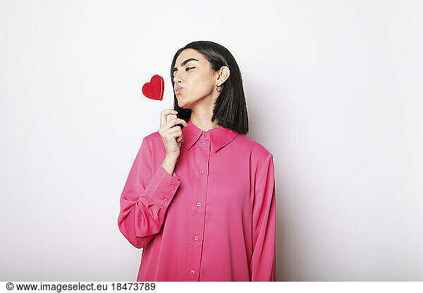 Young woman puckering at red heart shaped lollipop against white background