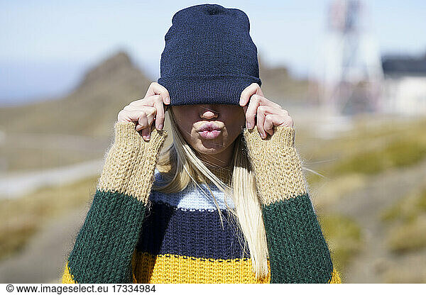 Young woman puckering while covering eyes with knit hat