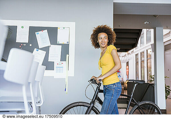 Young woman pushing bycicle in office