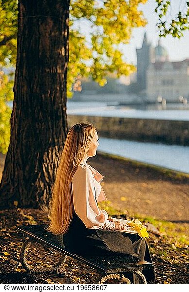 Young woman reading a book on the river bank in autumn Prague