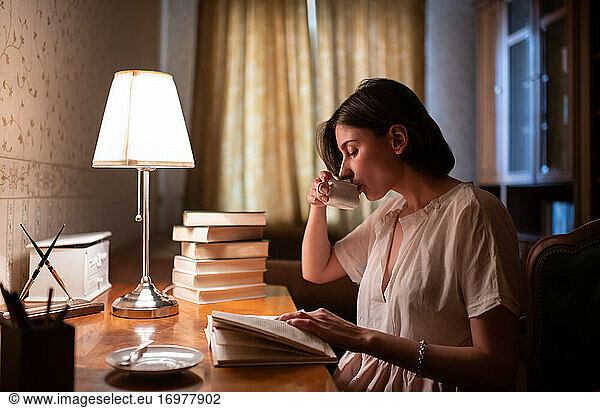 Young woman reading book and drinking hot beverage