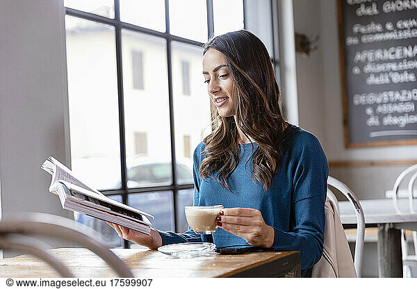 Young woman reading book and having coffee in cafe