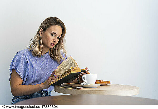 Young woman reading book at table in cafe