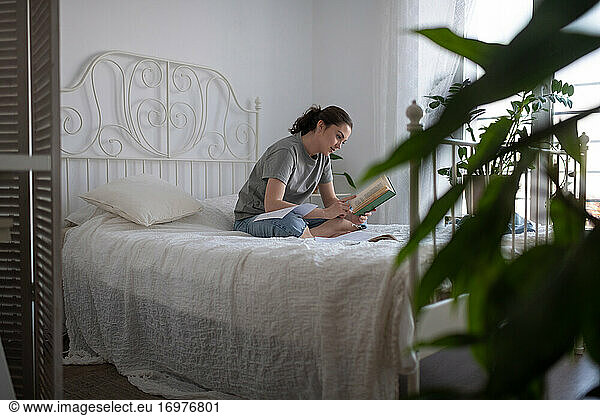 Young woman reading book during exam preparation at home