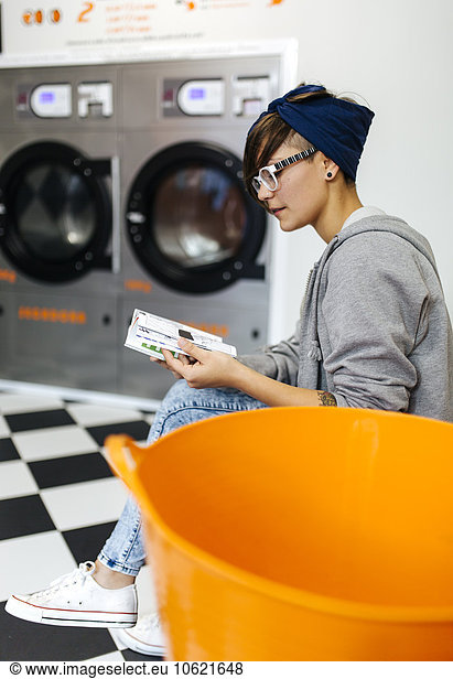Young woman reading comic strip in a launderette