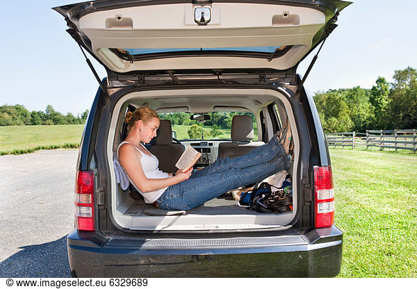 Young woman reading in back of sports utility vehicle