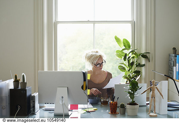 Young woman reading paperwork at desk in home office