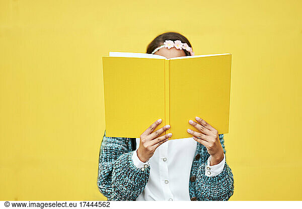 Young woman reading yellow book by wall