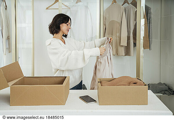Young woman recycling clothes with box on table at home