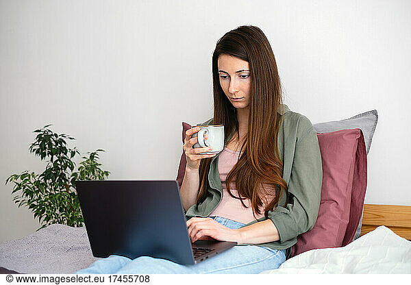 Young woman relaxing at home  using laptop and drinking coffee.