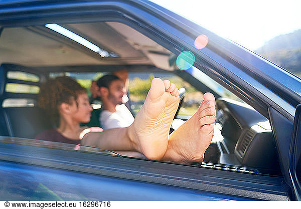 Young woman relaxing with bare feet out car window