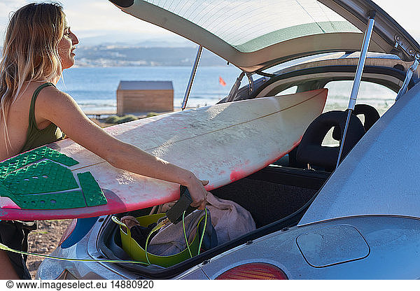 Young woman removing surfboard from car boot
