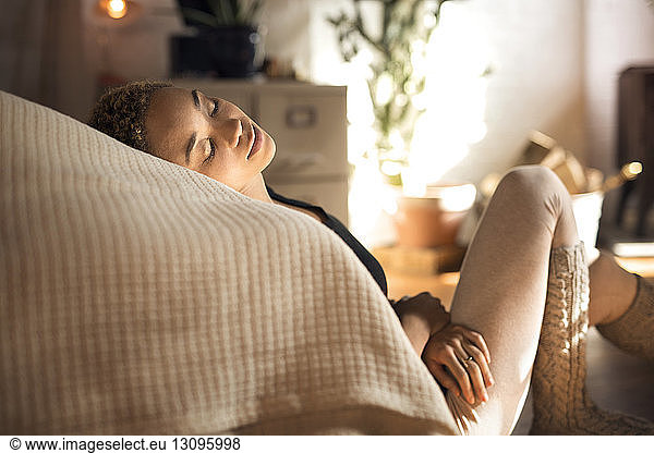 Young woman resting head on bed while sitting on floor at home