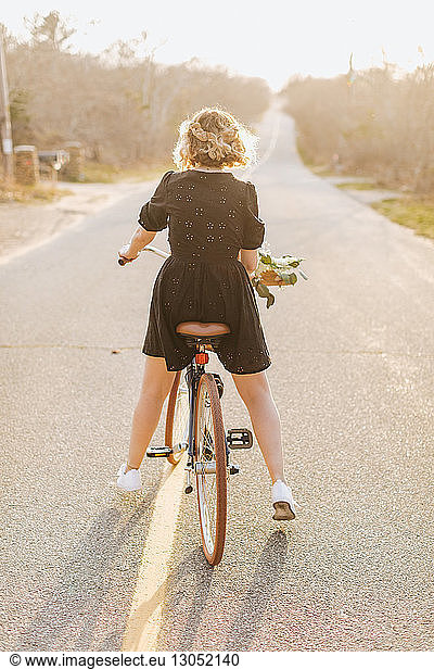 Young woman riding bicycle on rural road, rear view, Menemsha, Martha's Vineyard, Massachusetts, USA, Young woman riding bicycle on rural road, rear view, Menemsha, Martha's Vineyard, Massachusetts, USA