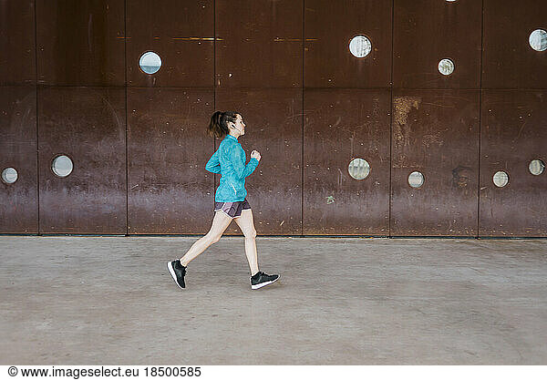 Young woman running along concrete wall in the city