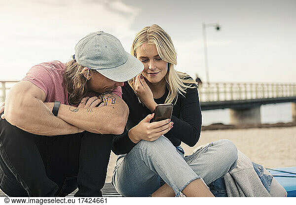 Young woman sharing smart phone with male friend at beach
