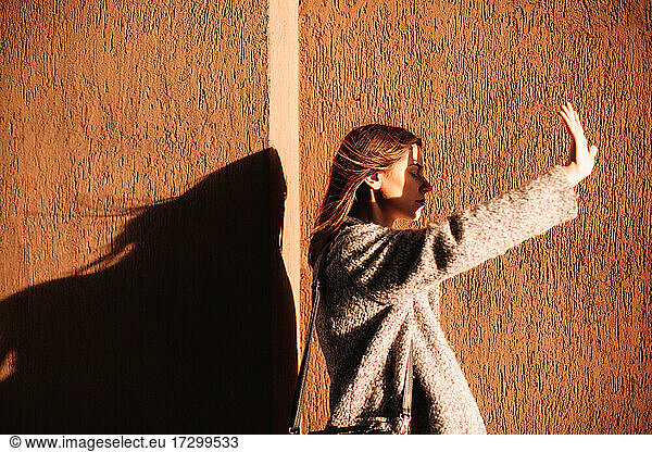 Young woman shielding eyes blocking sun against wall in city
