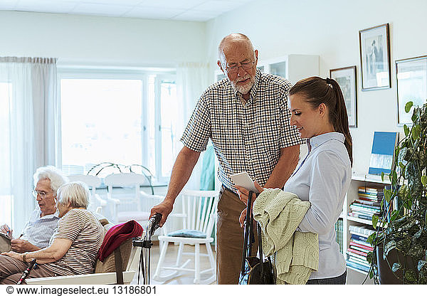 Young woman showing mobile phone to senior man at nursing home