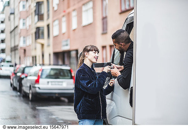 Young woman signing on smart phone being held by male mover in truck