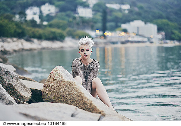 Young woman sitting alone on harbor rocks
