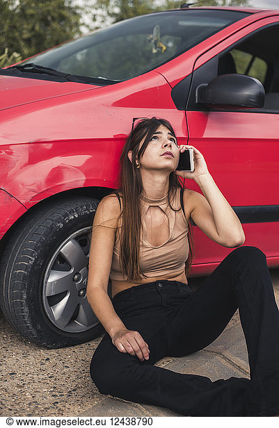 Young woman sitting at roadside having a car breakdown calling breakdown service