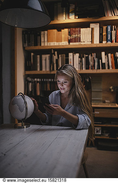 Young woman sitting at table with smartphone and globe