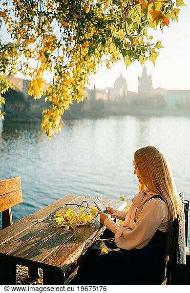 Young woman sitting at the table and looking at the phone in Prague