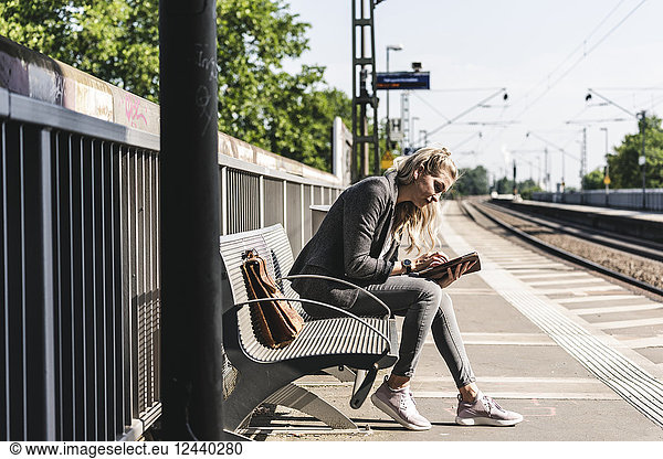 Young woman sitting at train station  using digital tablet