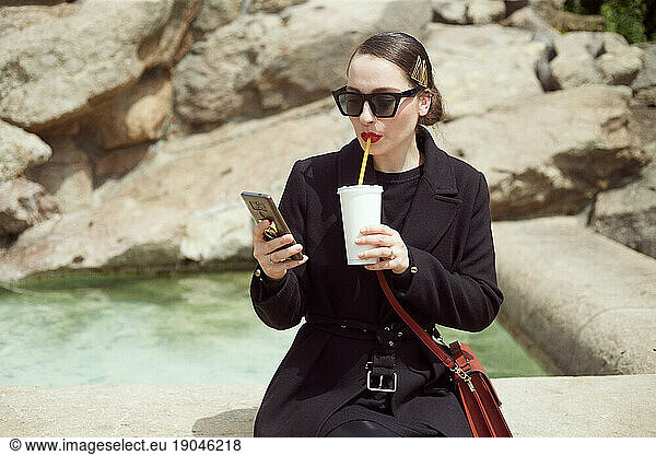 Young woman sitting by the fountain and drinking soda