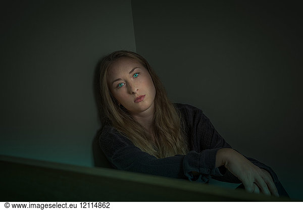 Young woman sitting in a corner with intense green eyes looking at the camera