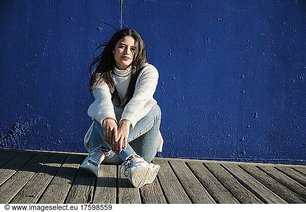 Young woman sitting in front of blue wall