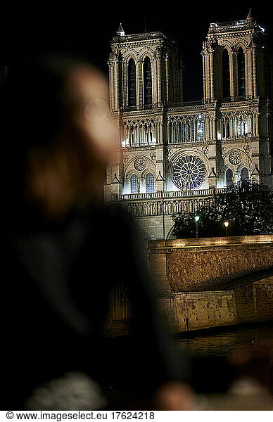 Young woman sitting in front of Notre Dame de Paris at night