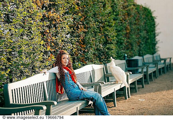 Young woman sitting on a bench next to a peacock in a park in Prague