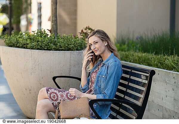 Young woman sitting on bench talking on phone