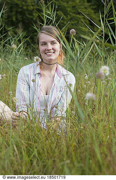 Young woman sitting on meadow and smiling  Bavaria  Germany