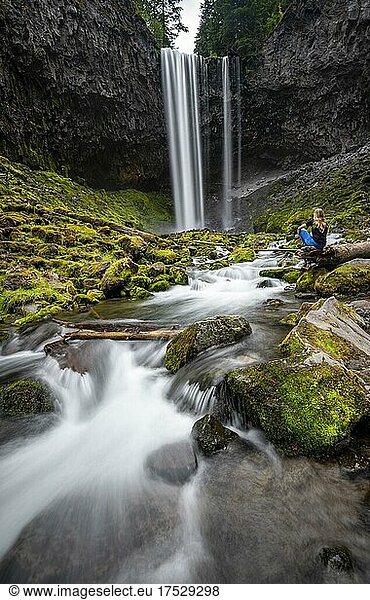 Young woman sitting on riverbank  waterfall cascading over ledge  Tamanawas Falls  long exposure  Cold Spring Creek wild river  Oregon  USA  North America