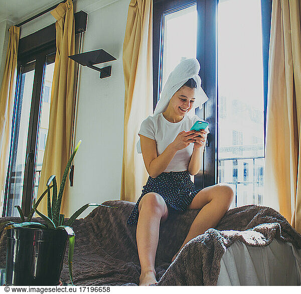 young woman sitting on the sofa with towel on her head looking mobile