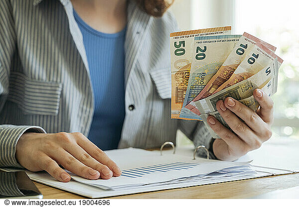Young woman sitting with financial documents and currency at home