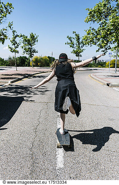 Young woman skateboarding along meridian srtip of empty road  rear view