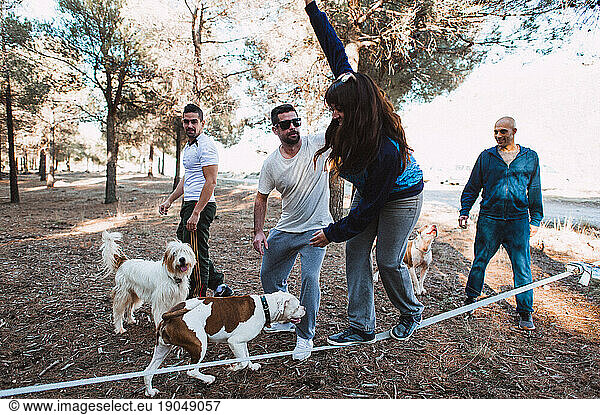 Young woman slacklining in forest with friends and dogs on sunny day