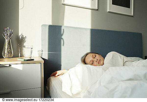Young woman sleeping in bed by table at home