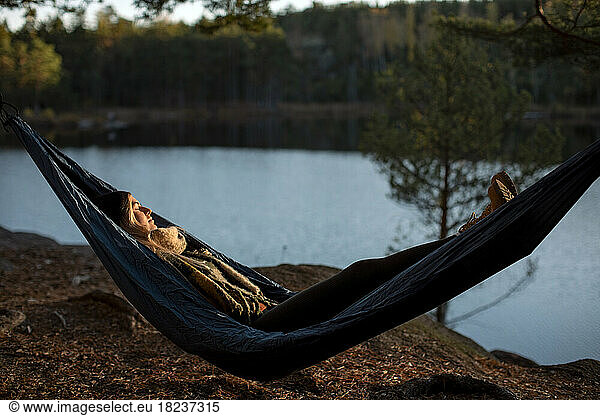 Young woman sleeping on hammock at lakeshore during sunset