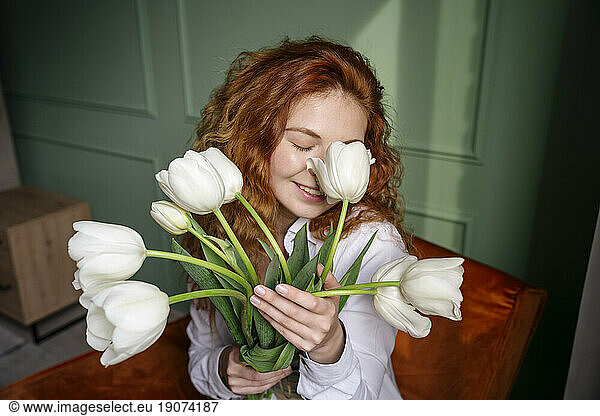 Young woman smelling bunch of tulip flowers at home
